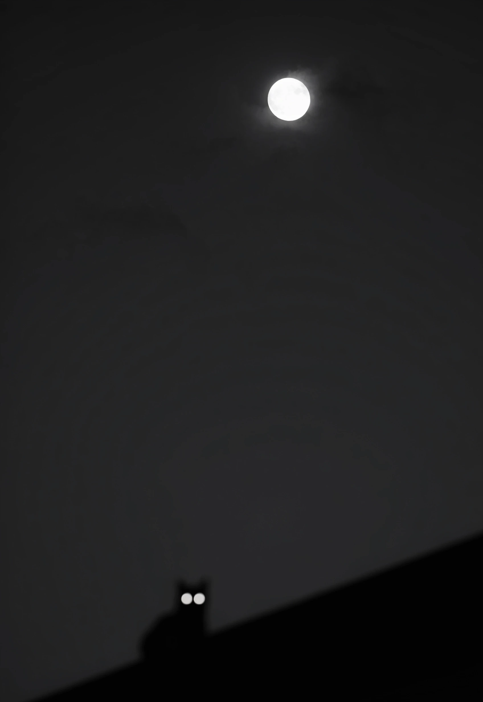 A cinematic hyper-realistic black and white minimalist shot dominated by a vast smooth night sky. High in the upper centre a sharp luminous full moon breaks through faint dark…